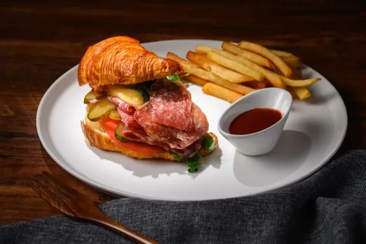 A croissant sandwich with sliced charcuterie, served with fries.